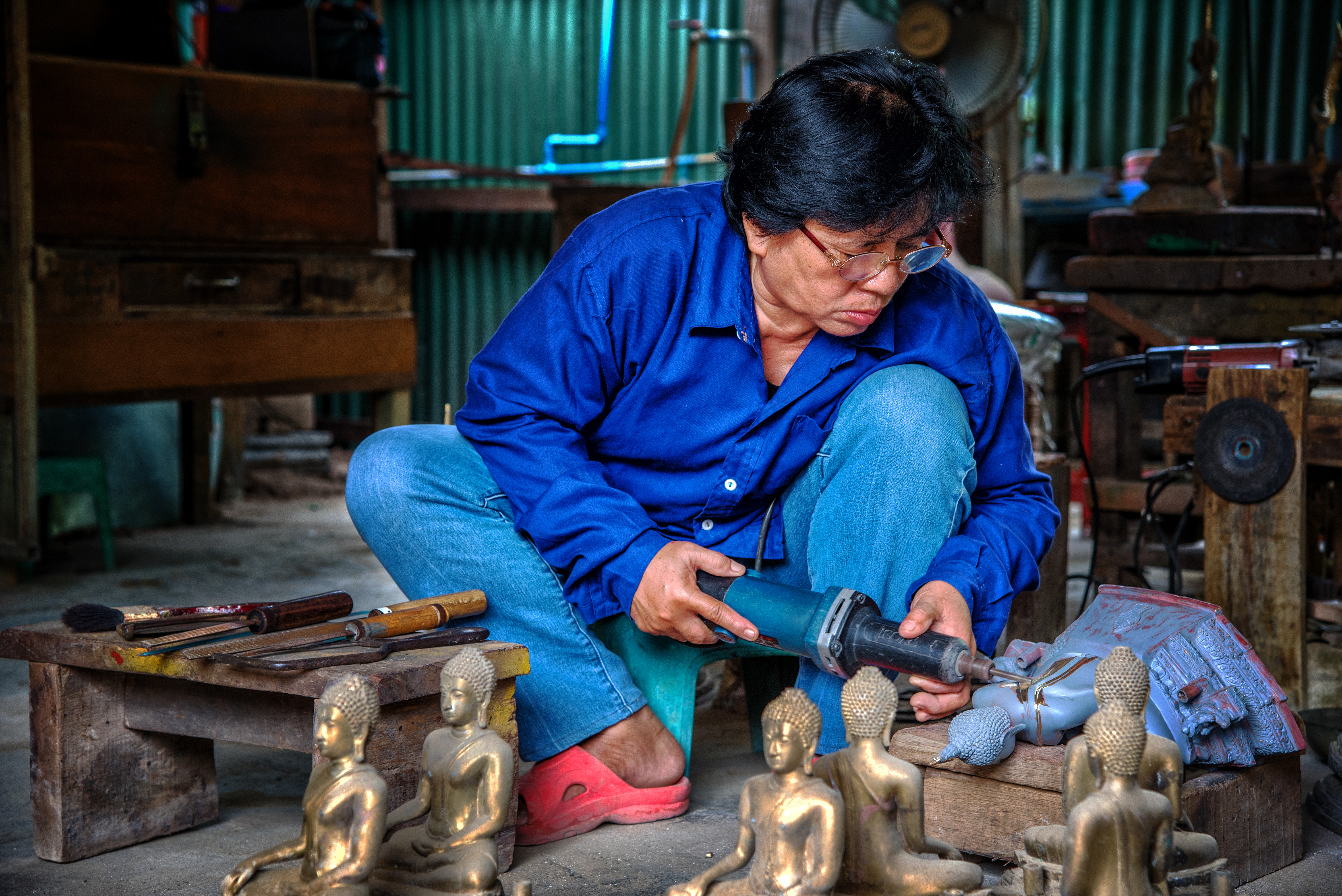 A worker at Buranathai Buddha Image Foundry  removes rough edges from a bronze Buddha Image, Phitsanulok, Thailand