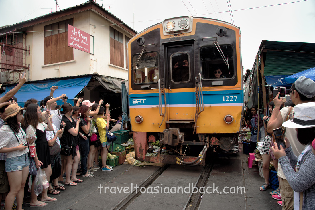 A train passes through the Maeklong Railway market, Samut Songkhram Province Thailand
